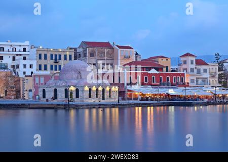 Vista del Porto Vecchio della città di Chania, dell'isola di Creta, con le sue case dai colori vivaci, il vecchio hamman in primo piano e luci riflesse sull'acqua setosa Foto Stock