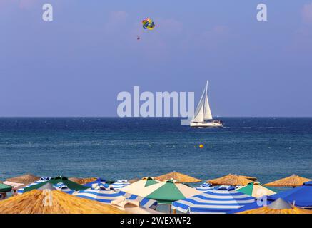 Ombrelloni multicolore sulla spiaggia di Rodi sullo sfondo di un cielo blu del mare e di uno yacht a vela. Grecia. Foto Stock