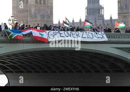 Londra, Regno Unito. 27 gennaio 2024. I sostenitori della Palestina drappeggiano una grande bandiera palestinese e uno striscione con la scritta "Game Over Sionism" sul lato del Westminster Bridge come parte di una giornata nazionale di azione che chiede un cessate il fuoco a Gaza. Crediti: Ron Fassbender/Alamy Live News Foto Stock