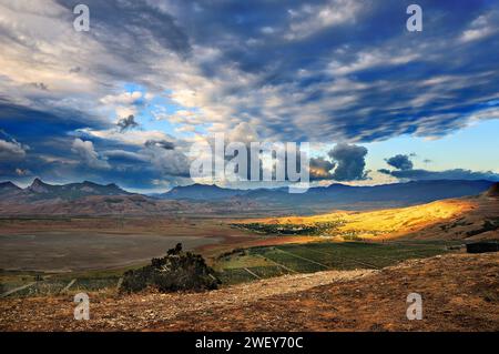 Il paesaggio montuoso al mattino presto. Le nuvole espresse in modo luminoso sopra la valle di montagna con il villaggio illuminato dai raggi del sole Foto Stock