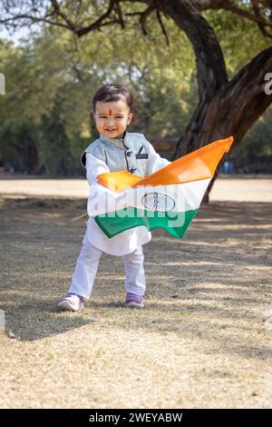 grazioso bambino indiano con bandiera nazionale indiana che cammina all'aperto in abiti tradizionali al mattino Foto Stock