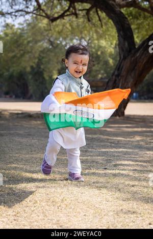 grazioso bambino indiano con bandiera nazionale indiana che cammina all'aperto in abiti tradizionali al mattino Foto Stock