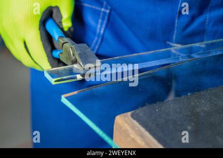 Un vetraio rompe a mano un piccolo pezzo di vetro spesso utilizzando un demolitore specializzato, lavora in una fabbrica di vetro, da vicino Foto Stock