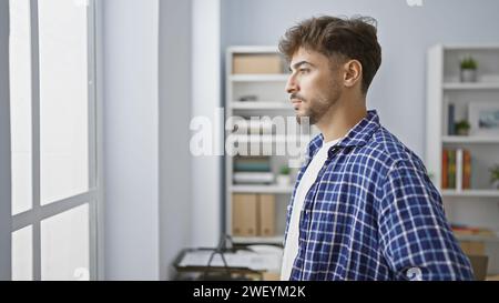 Giovane e di successo lavoratore d'affari arabo, rilassato guardando al chiuso dalla finestra del suo ufficio, immerso in un pensiero profondo mentre si occupa di un serio Foto Stock