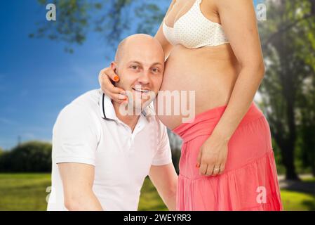 Un uomo gioioso abbraccia con tenerezza la moglie incinta sotto il cielo estivo, mentre condividono un bacio amorevole e si tengono i vestiti l'uno dell'altro in anticipo Foto Stock