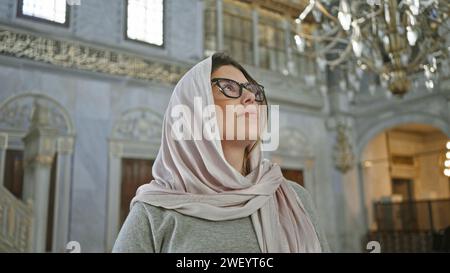 Una donna contemplativa in un hijab ammira l'interno decorato di una moschea di istanbul. Foto Stock