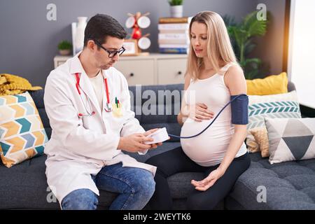 Uomo e donna medico e paziente incinta che hanno una consultazione medica utilizzando il tensiometro a casa Foto Stock