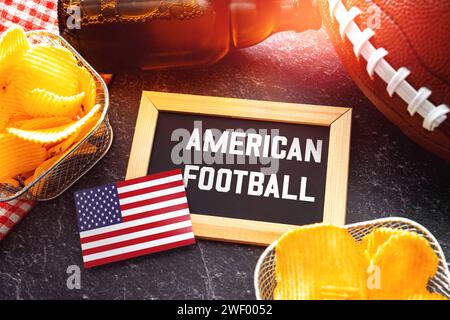 27 gennaio 2024: Lettere di football americano su una lavagna circondata da un football marrone, spuntini e birra. Sport americano FOTOMONTAGE *** American Football Schriftzug auf einer Tafel umgeben von einem braunen Football, Snacks und Bier. Amerikanischer Sport FOTOMONTAGE Foto Stock