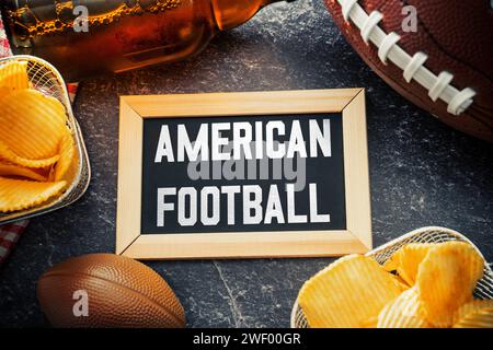 27 gennaio 2024: Lettere di football americano su una lavagna circondata da un football marrone, spuntini e birra. Sport americano FOTOMONTAGE *** American Football Schriftzug auf einer Tafel umgeben von einem braunen Football, Snacks und Bier. Amerikanischer Sport FOTOMONTAGE Foto Stock