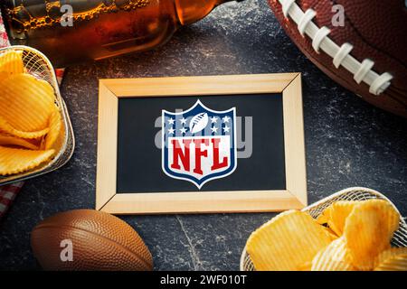 27 gennaio 2024: Logo della NFL National Football League su un tabellone circondato da un FOTOMONTAGGIO di football americano, spuntini e birra *** Logo della NFL National Football League auf einer Tafel umgeben von einem amerikanischen Football, Snacks und Bier FOTOMONTAGE Foto Stock