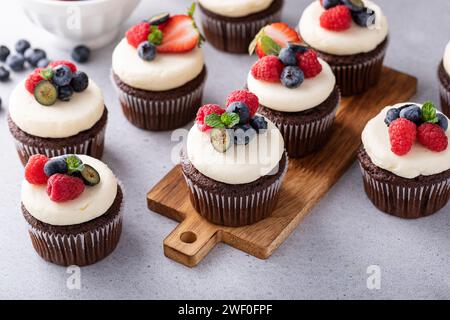 Cupcake al cioccolato con glassa alla vaniglia e frutti di bosco freschi Foto Stock
