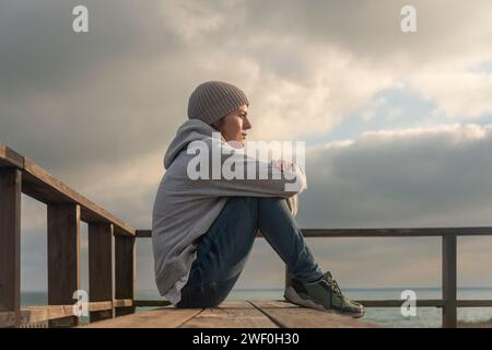 donna seduta su una panchina che guarda al mare, sola e premurosa Foto Stock