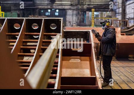 Lavoratore in maschera smeriglia una parte metallica in fabbrica o la taglia con una sega circolare elettrica. Foto Stock