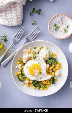 Colazione salutare con verdure cotte, broccoli, cavolfiore e mais e uova fritte in cima Foto Stock