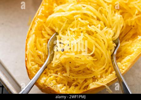 Spaghetti di zucca cotti al forno e tagliati a pezzi con due forchette, pronti da mangiare su una teglia da forno Foto Stock