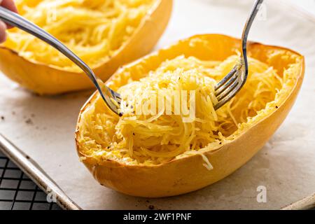 Spaghetti di zucca cotti al forno e tagliati a pezzi con due forchette, pronti da mangiare su una teglia da forno Foto Stock