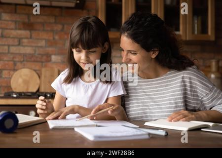 Giovane insegnante che fa da tutoratrice a una piccola allieva alla lezione di casa Foto Stock