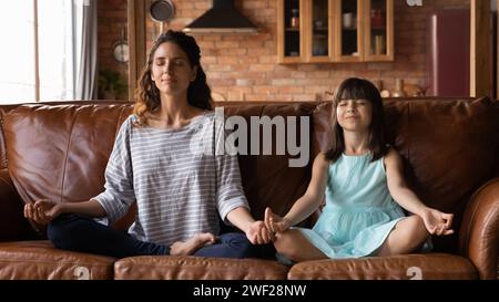 La madre ispanica e la bambina praticano l'esercizio yoga a casa Foto Stock