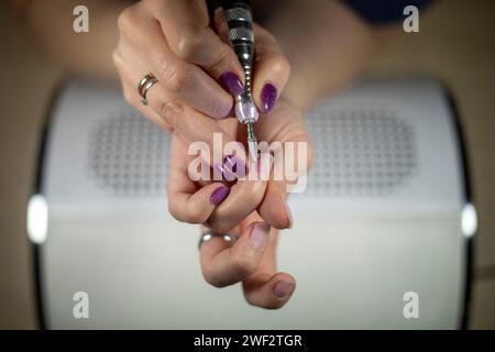 Primo piano dettagliato di cuticola caucasica irriconoscibile con lima per unghie elettrica sopra un collettore di polvere, manicure fai da te Foto Stock