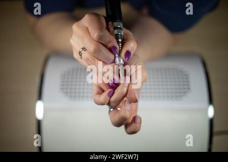 Primo piano dettagliato della cuticola di rimozione femminile irriconoscibile con lima elettrica su un collettore di polveri, primo piano della manicure fai da te Foto Stock