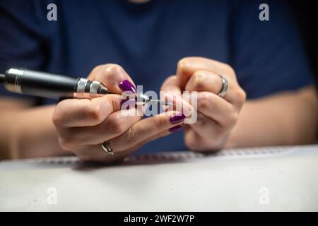 Primo piano dettagliato di una donna irriconoscibile che rimuove la cuticola dall'unghia con una lima elettrica per unghie sopra un collettore di polvere, manicure fai da te in primo piano Foto Stock