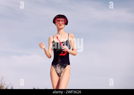 Donna sorridente che fa snorkeling in Red Fashion: Ritratto di una donna gioiosa che indossa un costume da bagno rosso, una maschera da snorkeling e un boccaglio, godendo la sua vacanza. Lei Foto Stock