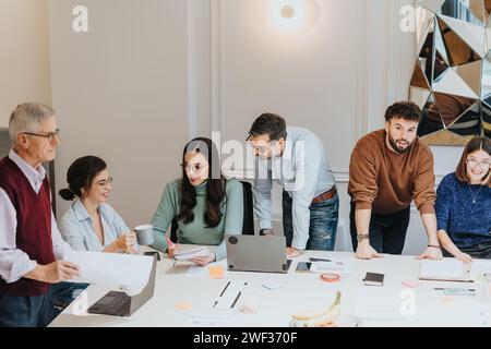 Un gruppo multigenerazionale di uomini e donne si riunisce intorno a un tavolo, collaborando a un incontro di lavoro incentrato sulla strategia e l'innovazione. Foto Stock