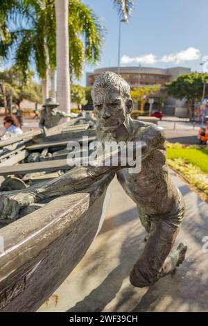 Una statua di bronzo di un pescatore maschio che spinge una piccola barca da pesca fuori dal mercato di Los Christianos. Foto Stock
