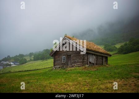 Una cabina abbandonata con un tetto vivente si erge su una collina a Loen, in Norvegia, durante una giornata nuvolosa e ricoperta. Foto Stock
