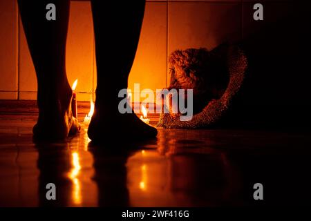 Orsacchiotto marrone sul pavimento con un cappello e gambe femminili nelle vicinanze al buio con candele, una casa e un giocattolo per bambini Foto Stock