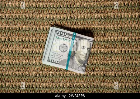 Banconote da cento dollari sotto una fascia elastica su un fondo di paglia, affari e finanza, soldi Foto Stock