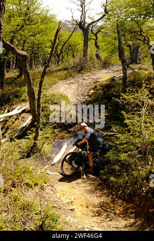 Un ciclista spinge la sua moto attraverso una sezione bagnata e fangosa della pista fino al Lago Desierto tra Candelario Mancilla in Cile e El Chalten in Argentina Foto Stock