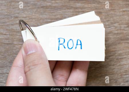 Tenere a mano una scheda flash con la scritta ROA (abbreviazione di Return on Assets) su sfondo di legno Foto Stock