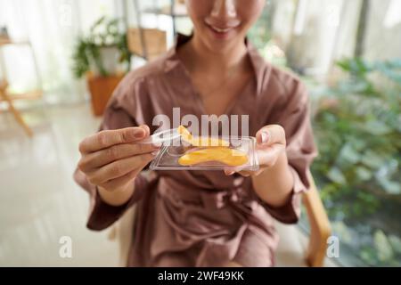 Giovane donna che prende sotto idrogel cerotti oculari dal pacchetto Foto Stock