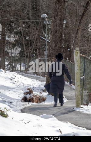Un ebreo ortodosso non identificato vestito di nero cammina su una strada tortuosa a New York durante l'inverno del 2024. Foto Stock