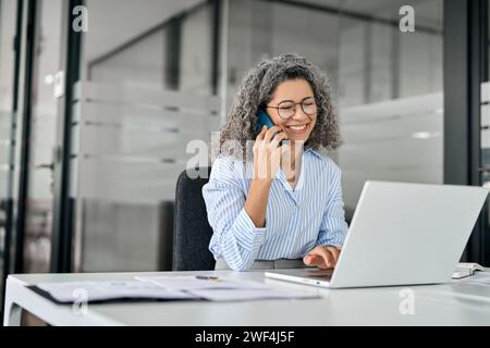 Donna d'affari matura sorridente che parla al telefono mentre fa una chiamata d'affari in ufficio. Foto Stock