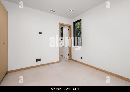 Una piccola camera minimalista con una grande porta e finestra, con pareti bianche pulite Foto Stock
