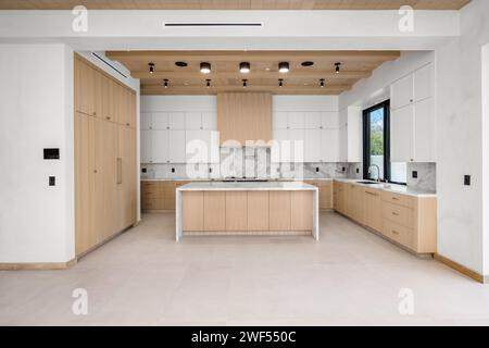 Spaziosa cucina bianca con eleganti accenti di legno e un'isola centrale Foto Stock