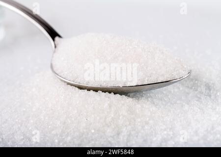 Zucchero bianco in cucchiaio d'argento su sfondo bianco Foto Stock