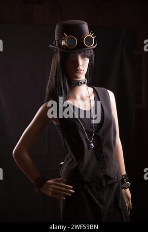 Manichino donna in plastica che indossa abiti e accessori steampunk in posa su sfondo nero con un effetto luce diviso Foto Stock