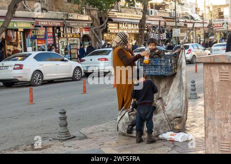 Rifugiati del Medio Oriente - una madre e i bambini che usano un carrello con una borsa mentre camminano attraverso la città di Sanliurfa in Turchia Foto Stock