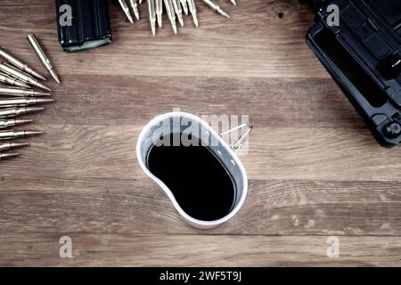 Cartucce e caffè nero. Fucili d'assalto con cartucce e tazza di caffè su fondo di legno. Foto Stock