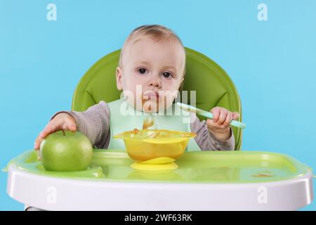 Piccolo bambino carino che mangia cibo sano in seggiolone su sfondo azzurro Foto Stock