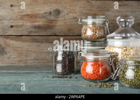 Diversi tipi di legumi e cereali in vasetti di vetro su tavola di legno blu, spazio per il testo. Grani organici Foto Stock