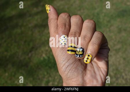 Creative Nail Art con tema Bee. Disegni per unghie, disegni per alveare con strisce, motivi a puntini sui colori giallo, bianco e nero Foto Stock