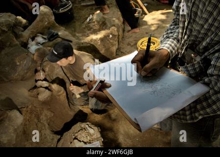 Il paleontologo Iwan Kurniawan disegna uno schizzo su carta che mostra le posizioni delle ossa fossilizzate di Elephas hysudrindicus, una specie di elefante estinta vissuta durante l'epoca del Pleistocene, che in seguito è conosciuta come "elefante Blora" mentre il suo team sta lavorando in background nel sito di scavo di Sunggun, Mendalem, Kradenan, Blora, Central Java, Indonesia. Il team di ricerca sui vertebrati (Agenzia geologica, Ministero dell'energia e delle risorse minerarie indonesiano) guidato dallo stesso Kurniawan con Fachroel Aziz ha scoperto le ossa della specie quasi interamente (circa il 90% completo). Foto Stock