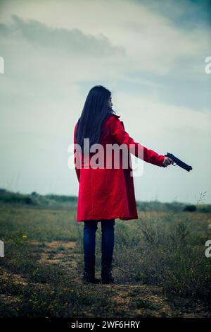 Vista posteriore di una donna in cappotto rosso che regge una pistola Foto Stock