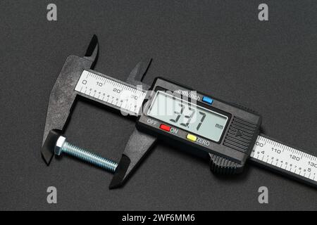 Misurazione della lunghezza del bullone con un calibro digitale. Fotografia macro su sfondo scuro Foto Stock