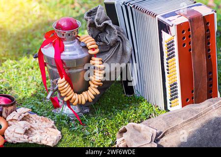 Composizione di picnic o Maslenitsa con bagel, samovar, scarpe Bast, fisarmonica a bottoni, borsa su erba verde. Shrovetide Foto Stock