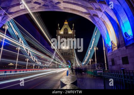 Una lunga esposizione notturna scattata sul Tower Bridge con un pedone, i turisti che visitano questo iconico monumento e i sentieri luminosi dai veicoli di passaggio. Foto Stock